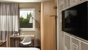 A hotel room with a bed, a desk with a chair, a television, a window with curtains, and a door. - ibis Coventry Centre (Coventry)