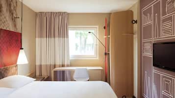 Quarto de hotel com cama, escrivaninha, cadeira, televisão e janela com cortinas.