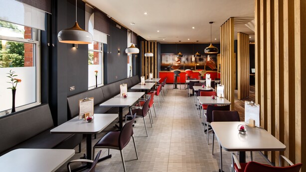 A modern restaurant interior with long tables, red chairs, and pendant lighting. - ibis Coventry Centre (Coventry)