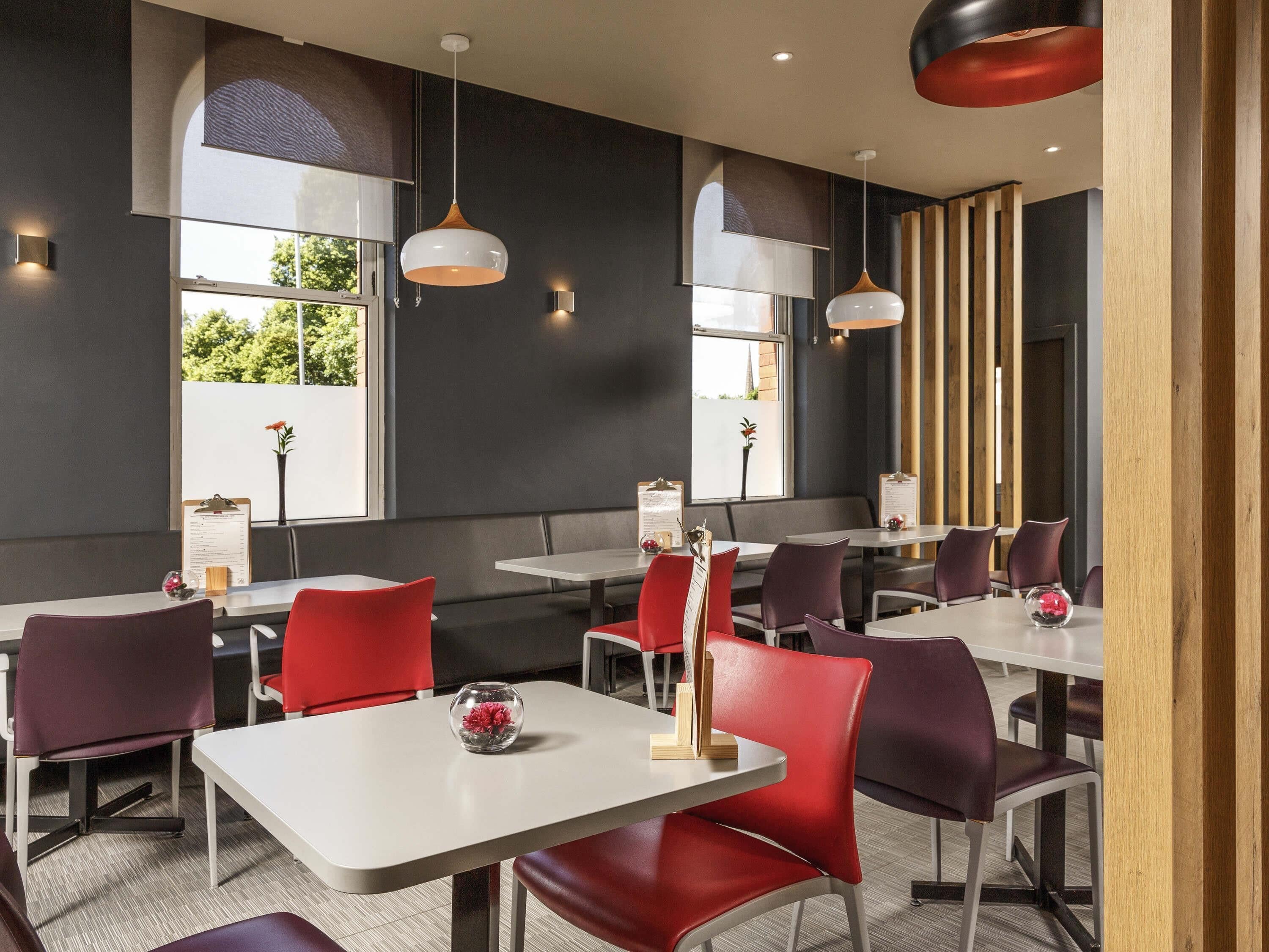L’intérieur d’un restaurant moderne, avec des tables blanches, des chaises rouges et violettes, des luminaires suspendus et de grandes fenêtres.