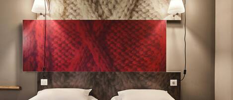 A hotel room with two beds, a large red and gray patterned wall, and two wall-mounted lamps.