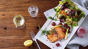 A plate of salmon with a side salad, a glass of white wine, and a lemon half on a wooden table. - ibis Coventry Centre (Coventry)