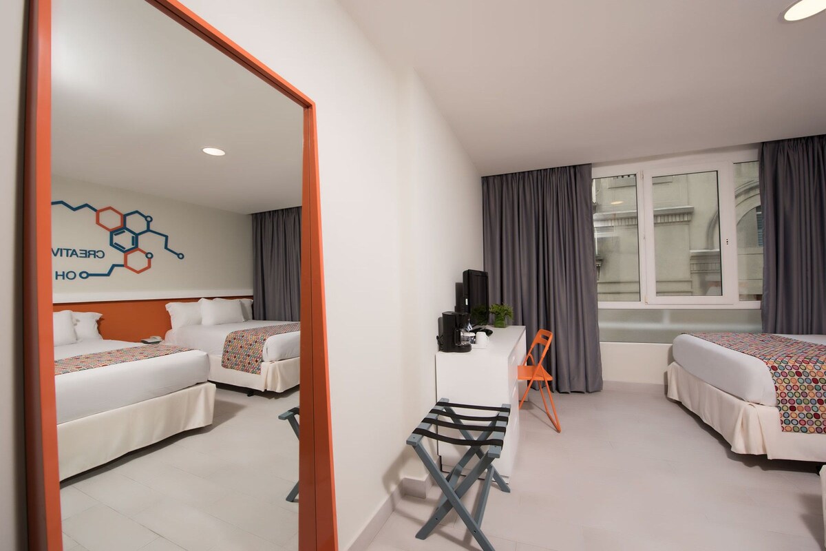 A hotel room with two beds, a desk with a chair, a mirror, and a window with curtains.