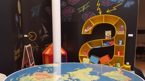 Una habitación con un globo terráqueo de puzzle grande, una estantería amarilla y una pared con dibujos coloridos.