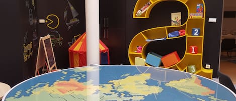 Quarto com um globo-mapa de encaixe grande, uma estante amarela e parede com desenhos coloridos.