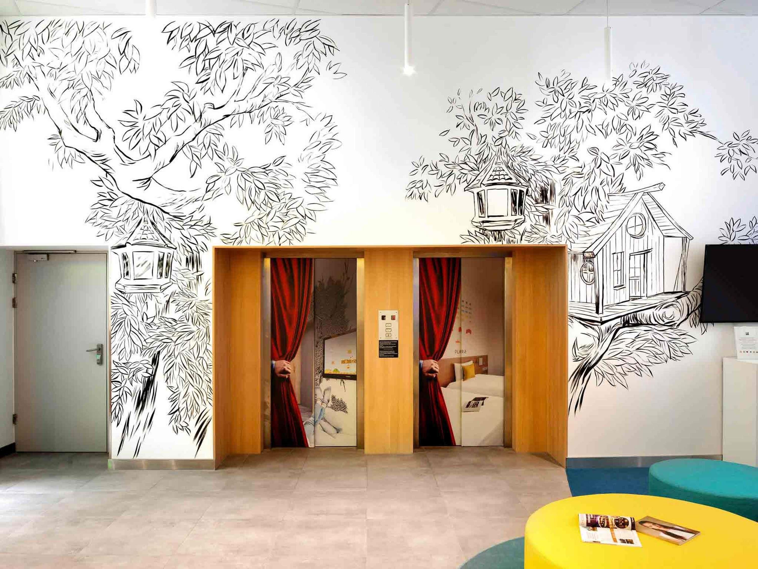 Une pièce avec une porte en bois, des rideaux rouges, un lit, un téléviseur et une fresque murale.