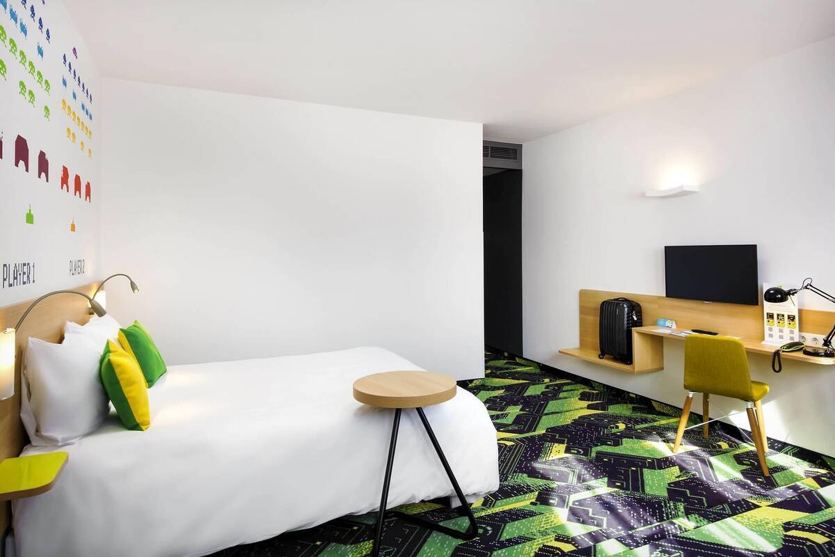 A hotel room with a bed, a desk, a chair, a television, and a wall with colorful icons.