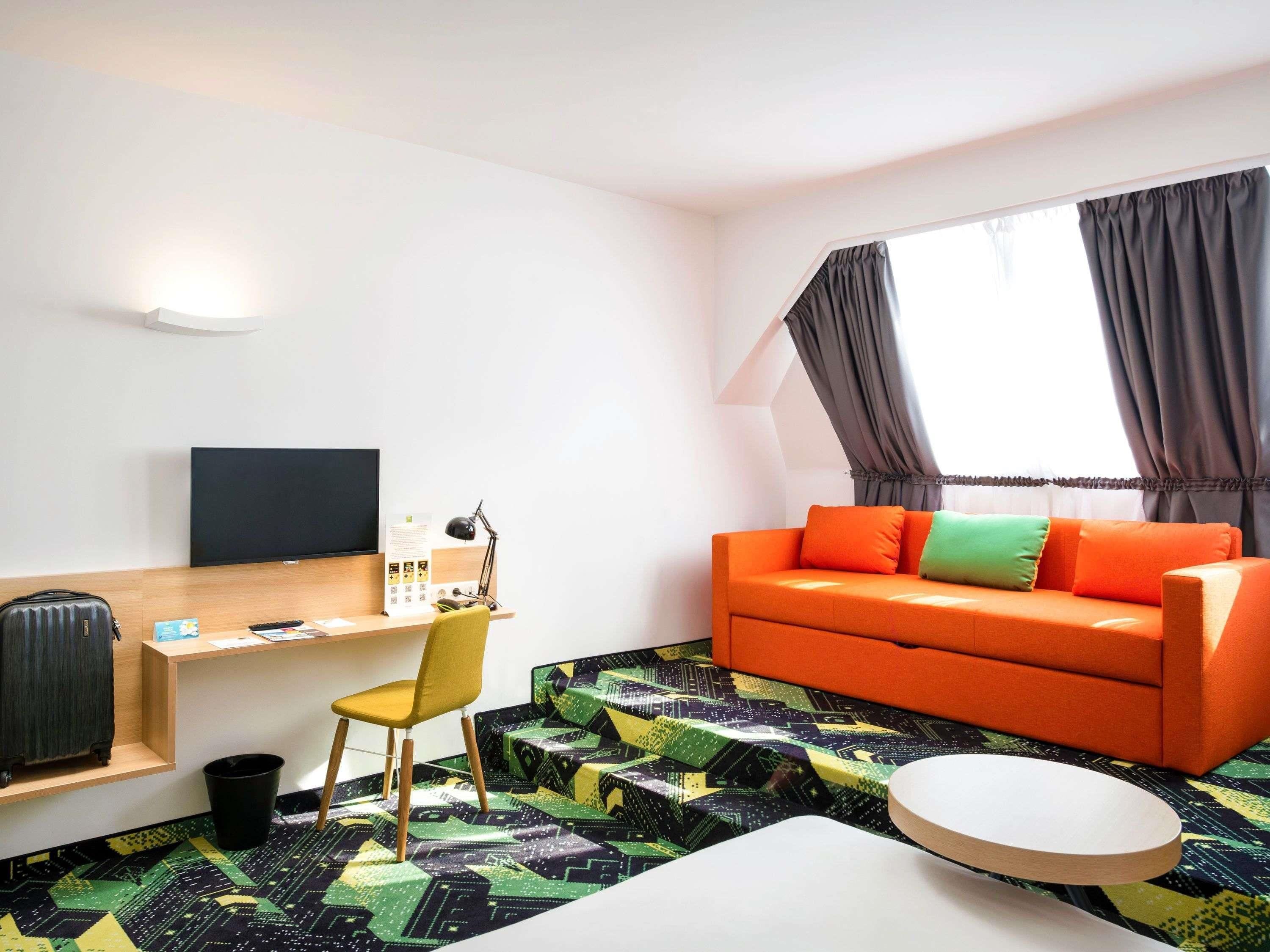 Une chambre d’hôtel moderne équipée d’un canapé, d’un bureau, d’une chaise, d’une télévision et d’un tapis à motifs.