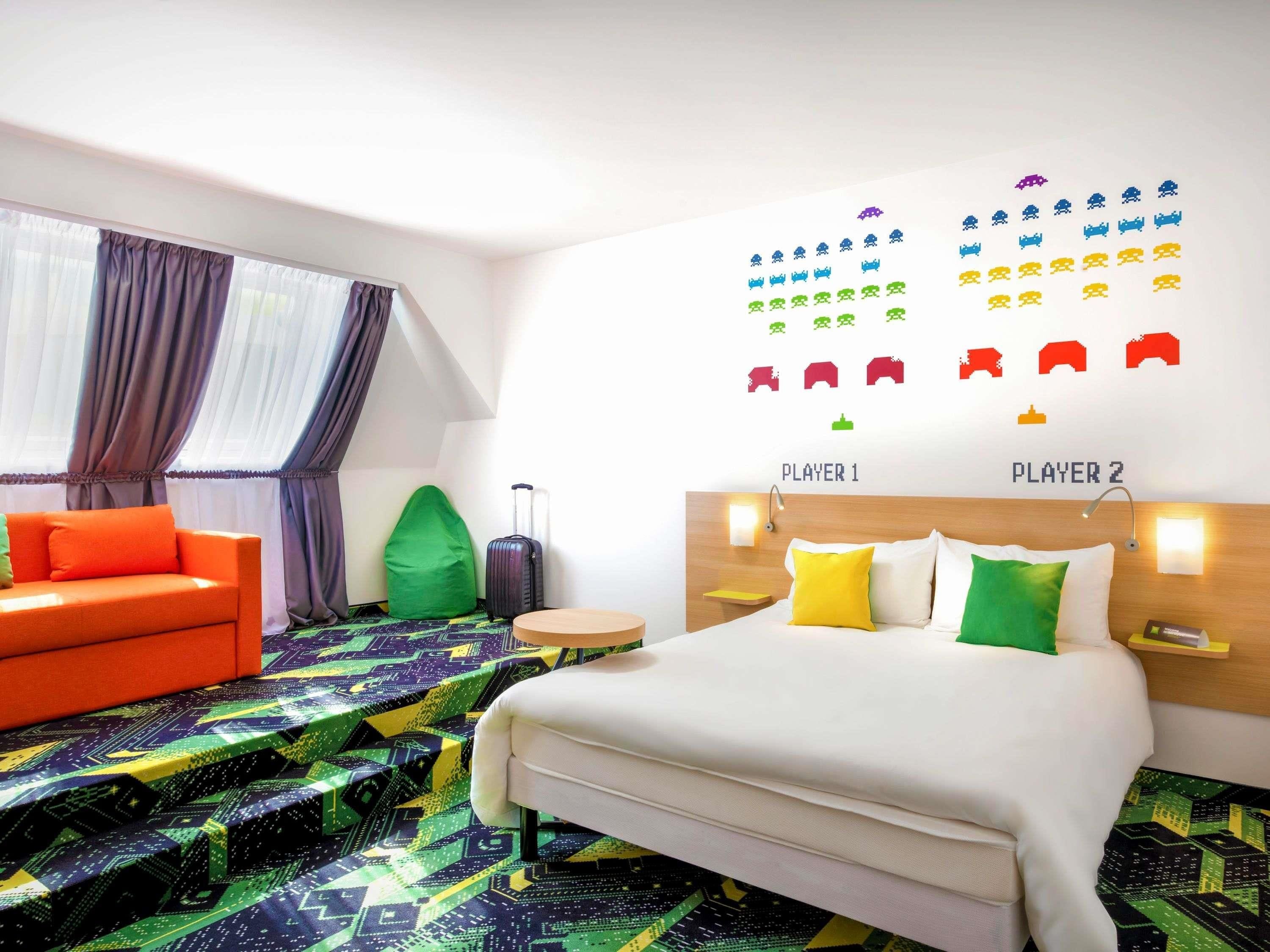 A hotel room with a bed, a sofa, a suitcase, and a wall with game icons.