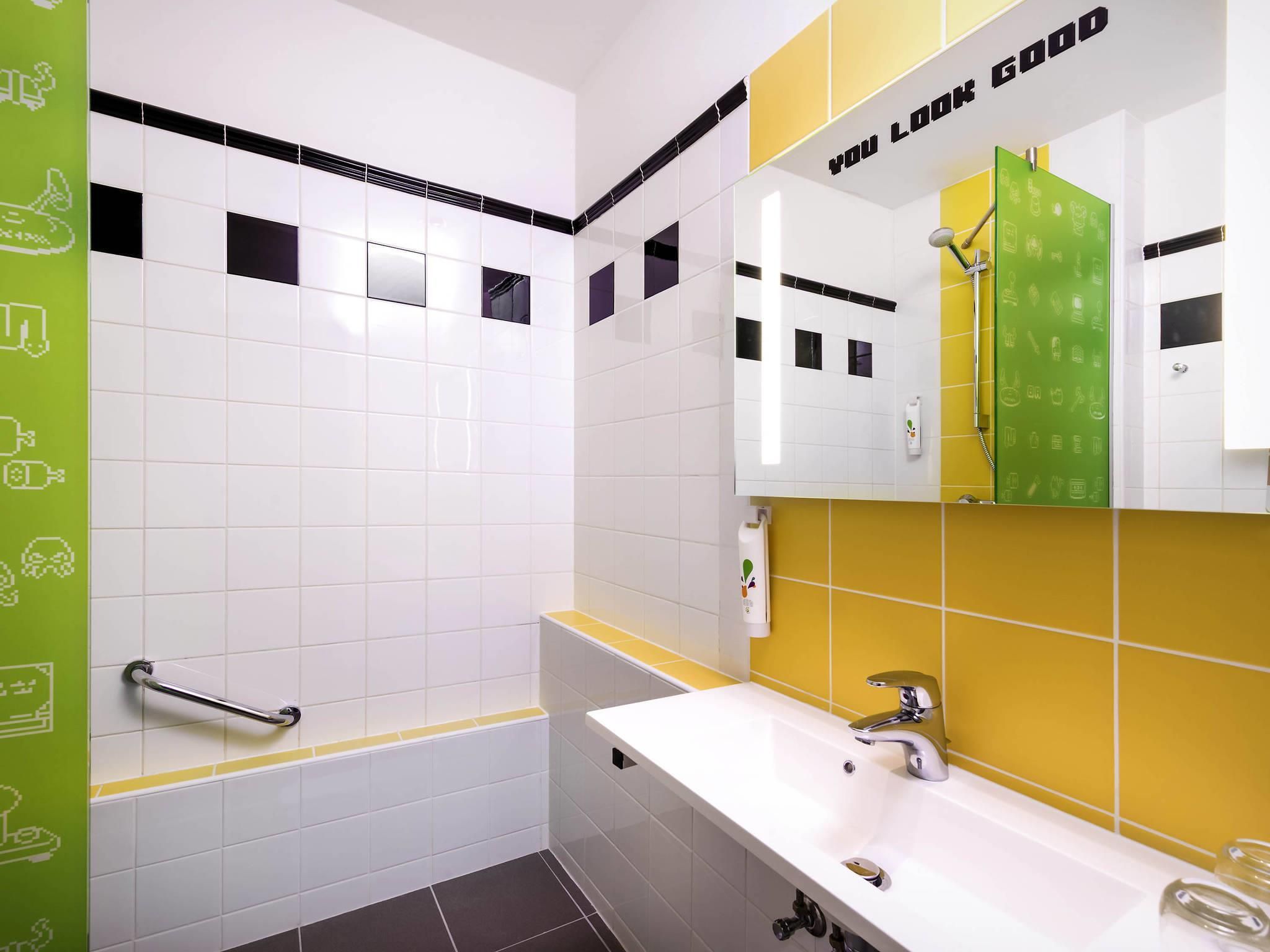A modern bathroom with white and yellow tiles, a mirror with a green cabinet, and a handrail.