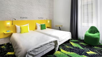 A hotel room with a white brick wall, two beds labeled 'PLAYER 1' and 'PLAYER 2', a green bean bag chair, and a patterned carpet.