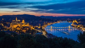 Un paisaje urbano al atardecer con edificios iluminados, un río y un puente.