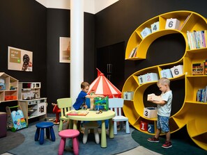 Un cuarto de juegos infantil con una gran estantería amarilla, una cocina de juguete y una mesa con taburetes.