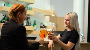 Two individuals holding glasses with drinks, a bar area with shelves of bottles and glasses, and a counter.