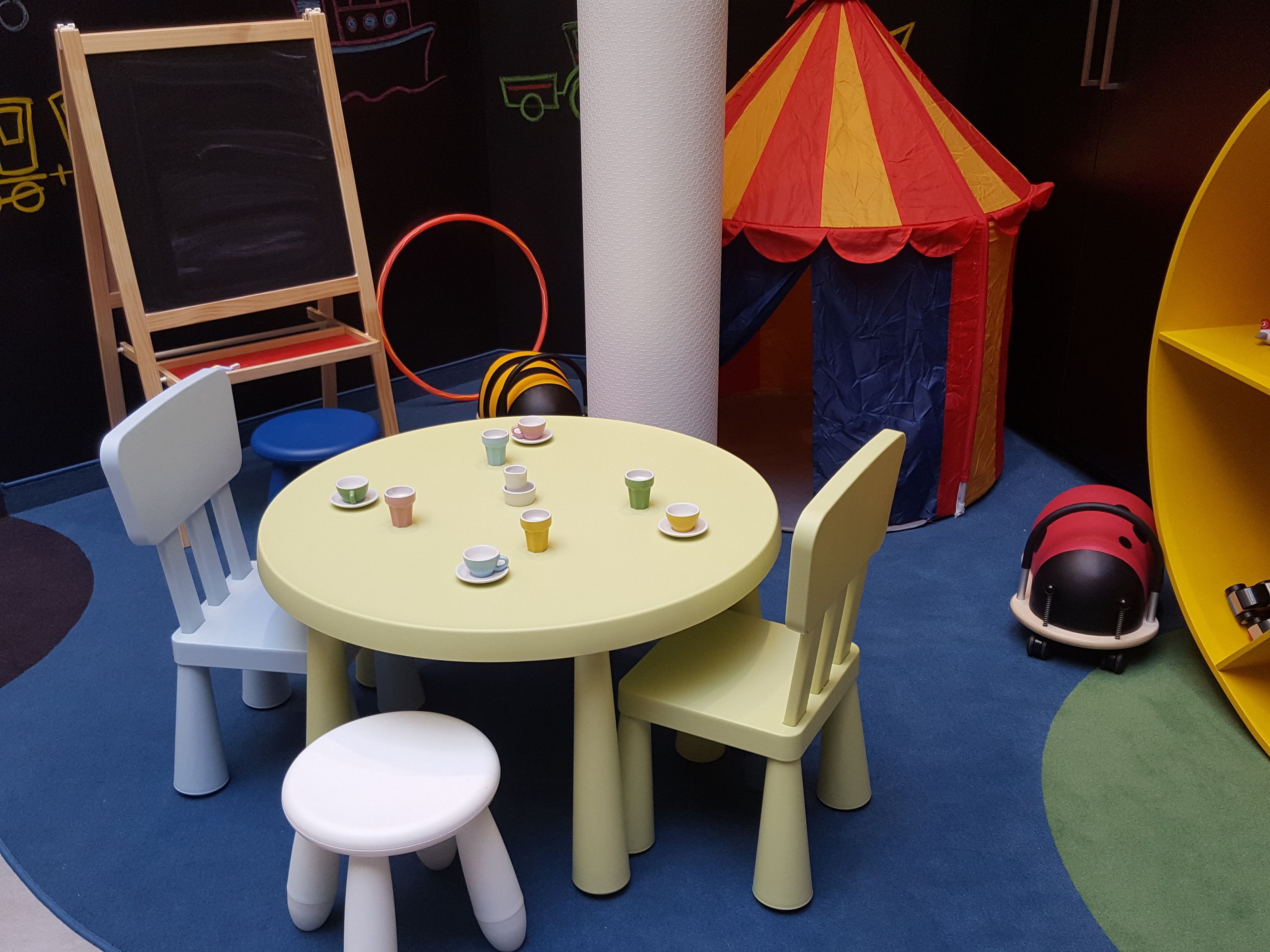 A children's play area with a round table, chairs, and a small chalkboard.