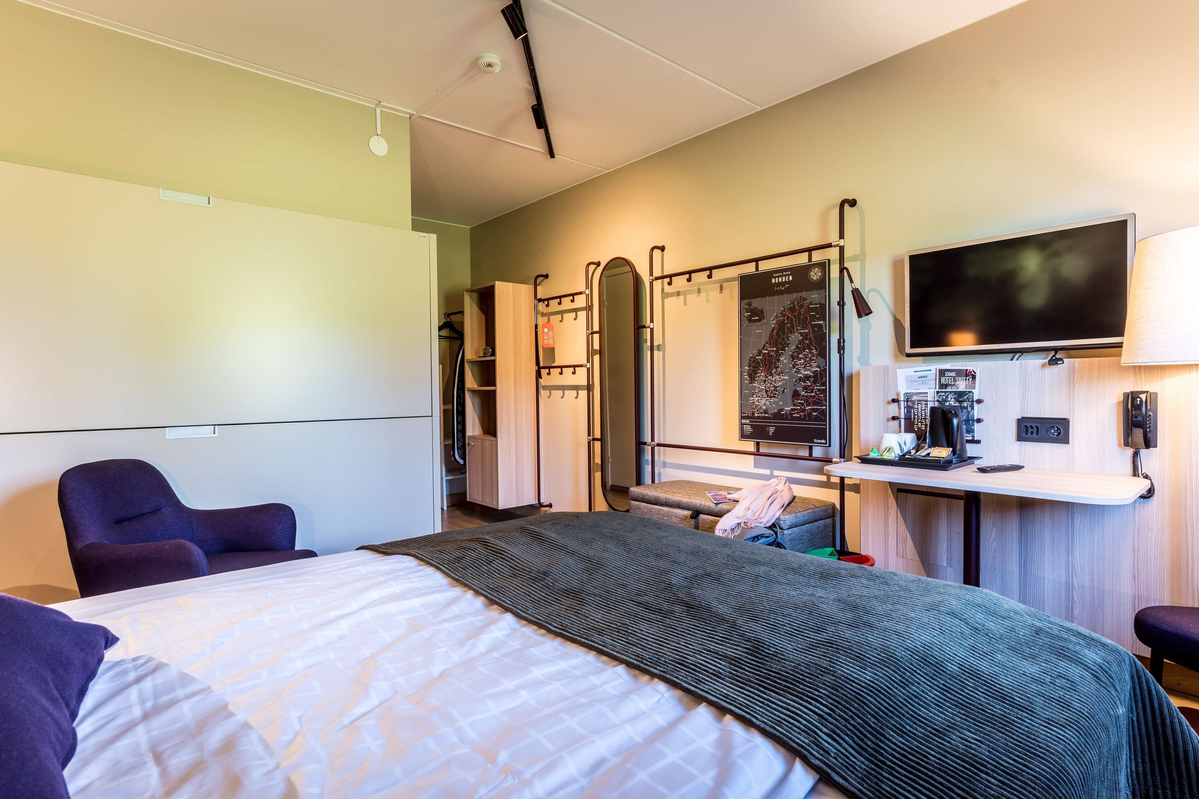 Habitación de hotel con una cama, un escritorio con computadora, un televisor y un espejo.