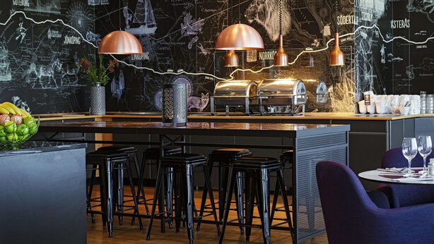 Zona de bar moderna con un revestimiento mural con motivos de mapa, taburetes y lámparas colgantes de cobre.