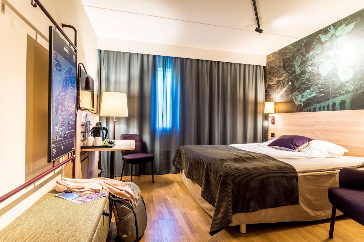 Une chambre d’hôtel avec un lit, un bureau doté d’une lampe, une chaise et une grande carte accrochée au mur.