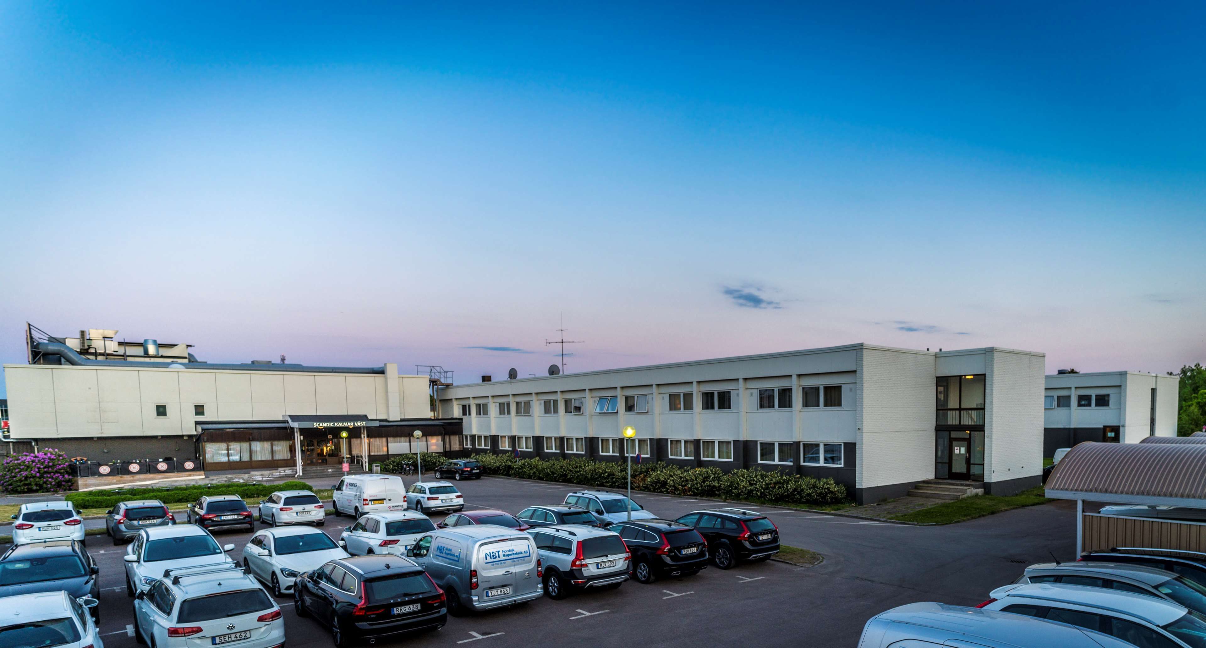 Ein Parkplatz mit mehreren Autos und einem Gebäude mit flachem Dach und großen Fenstern.