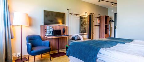 Una habitación de hotel con cama, escritorio con computadora, silla, televisor y armario.