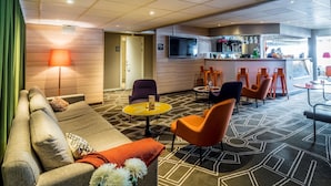 Un hall de hotel con sofá, sillones, una pequeña mesa, zona de bar y una pantalla de televisión.