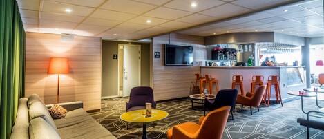 Un hall de hotel con sofá, sillones, una pequeña mesa, zona de bar y una pantalla de televisión.