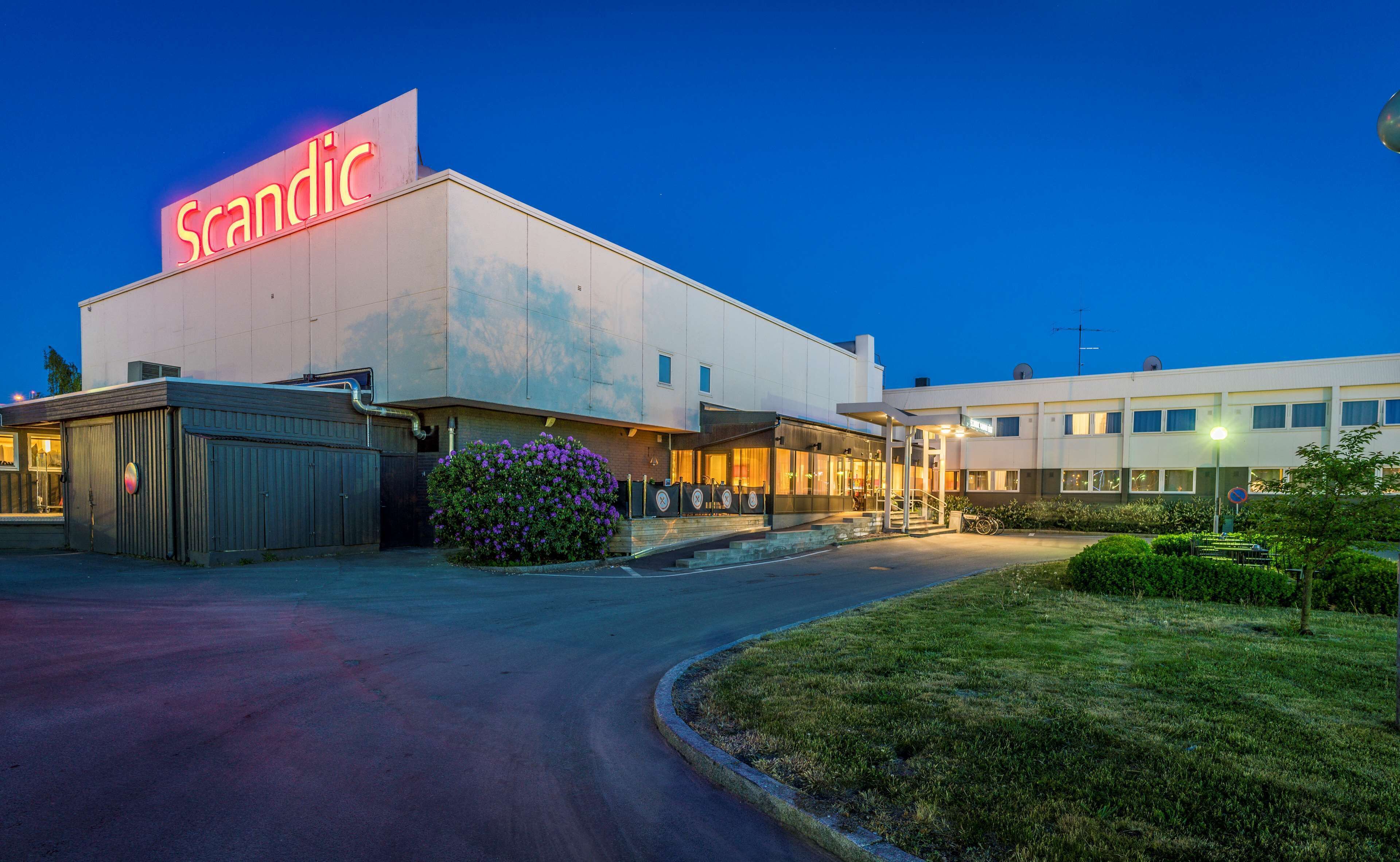 A building with a prominent 'Scandic' sign, a covered entrance, and a parking area.