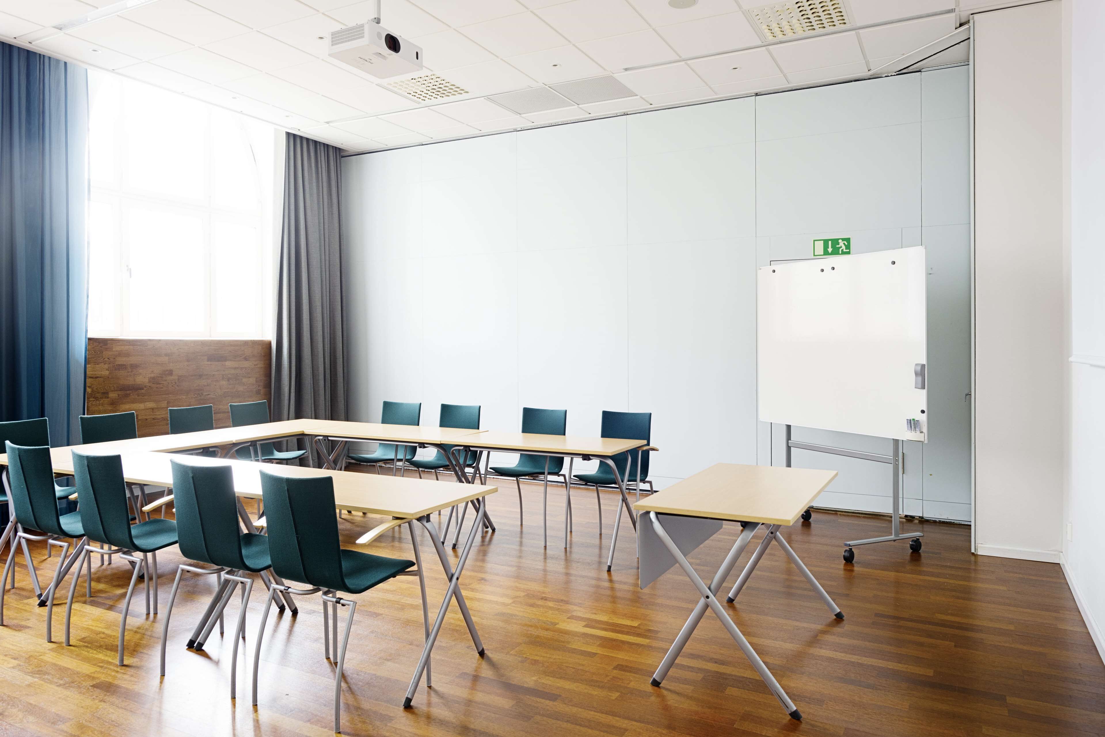 Una sala conferenze con un lungo tavolo, diverse sedie, una lavagna e un pavimento in legno.