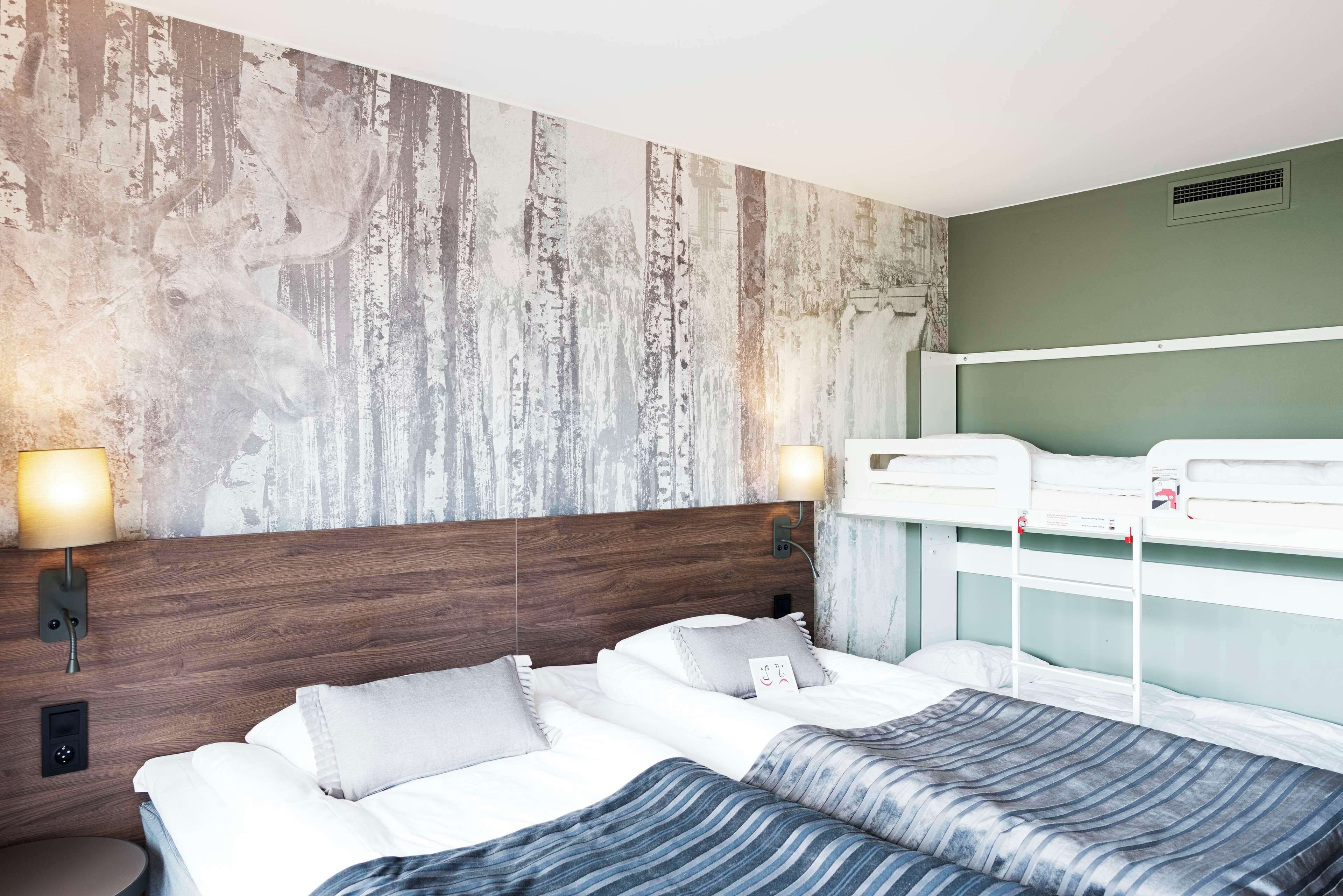 A hotel room with a wooden headboard, two beds, a large wall mural, and bedside lamps.