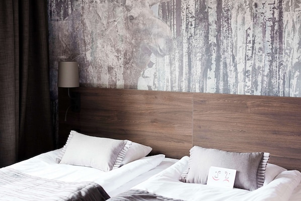 Habitación de hotel con cabecera de madera, dos camas con ropa blanca y un mural texturizado en la pared.