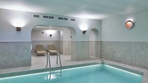 Una piscina interior moderna con agua cristalina, dos sillones de descanso e iluminación empotrada en el techo.