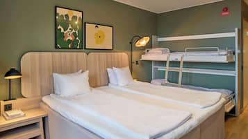 Un lit double avec une tête de lit en bois, une table de chevet avec une lampe, et un lit superposé sur le côté droit.