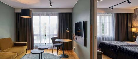 A hotel room with a sofa, a round table, a TV, and a bed.