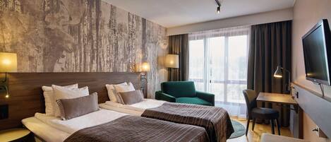 Quarto de hotel com duas camas, uma escrivaninha, uma cadeira, televisão e uma janela grande com cortinas.