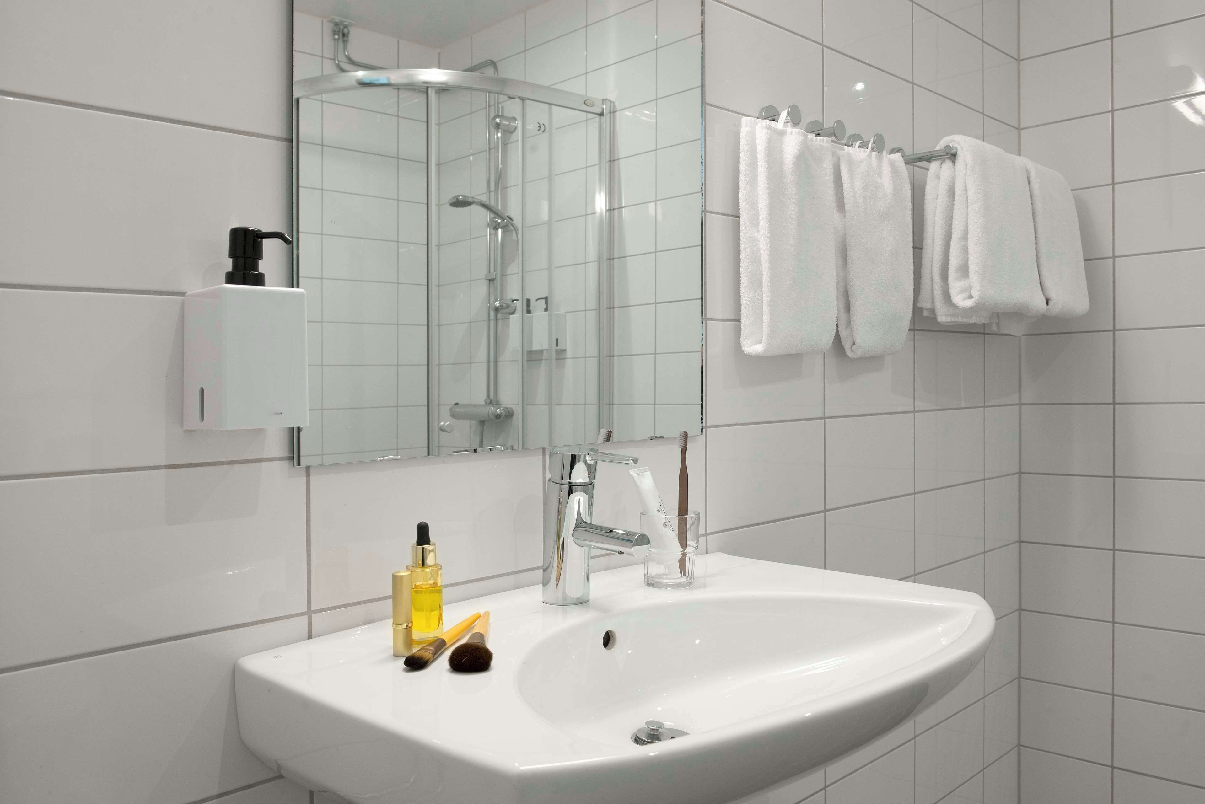 A modern bathroom with a white sink, a glass shower enclosure, and a towel rack with white towels.