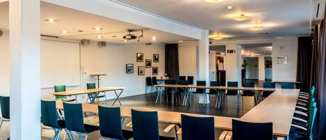 Une salle de conférence avec une longue table et des chaises, des murs blancs et des luminaires au plafond.