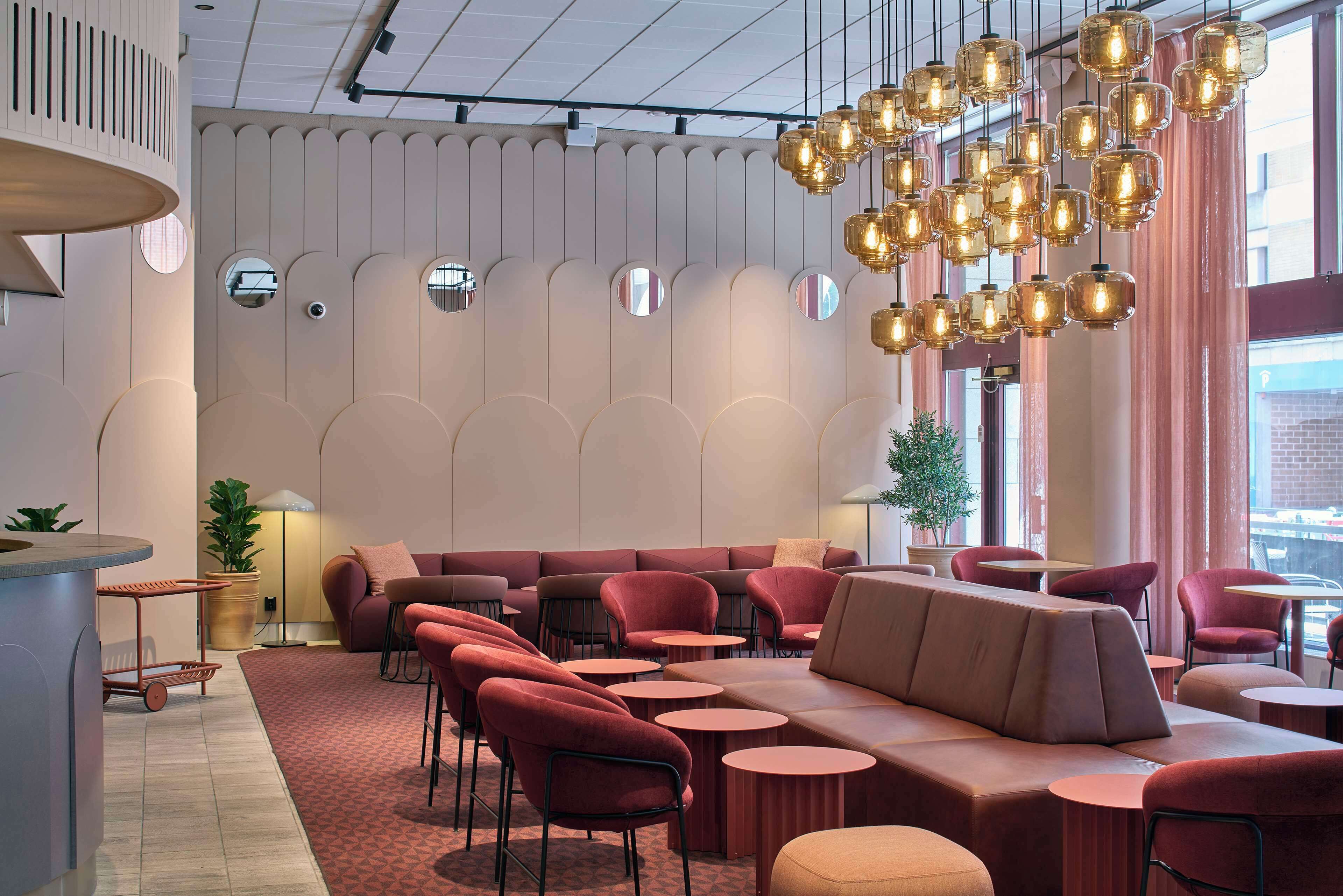 Een moderne lounge met een bank, stoelen en ronde tafels, met een bijzonder plafondontwerp inclusief hangende verlichting.