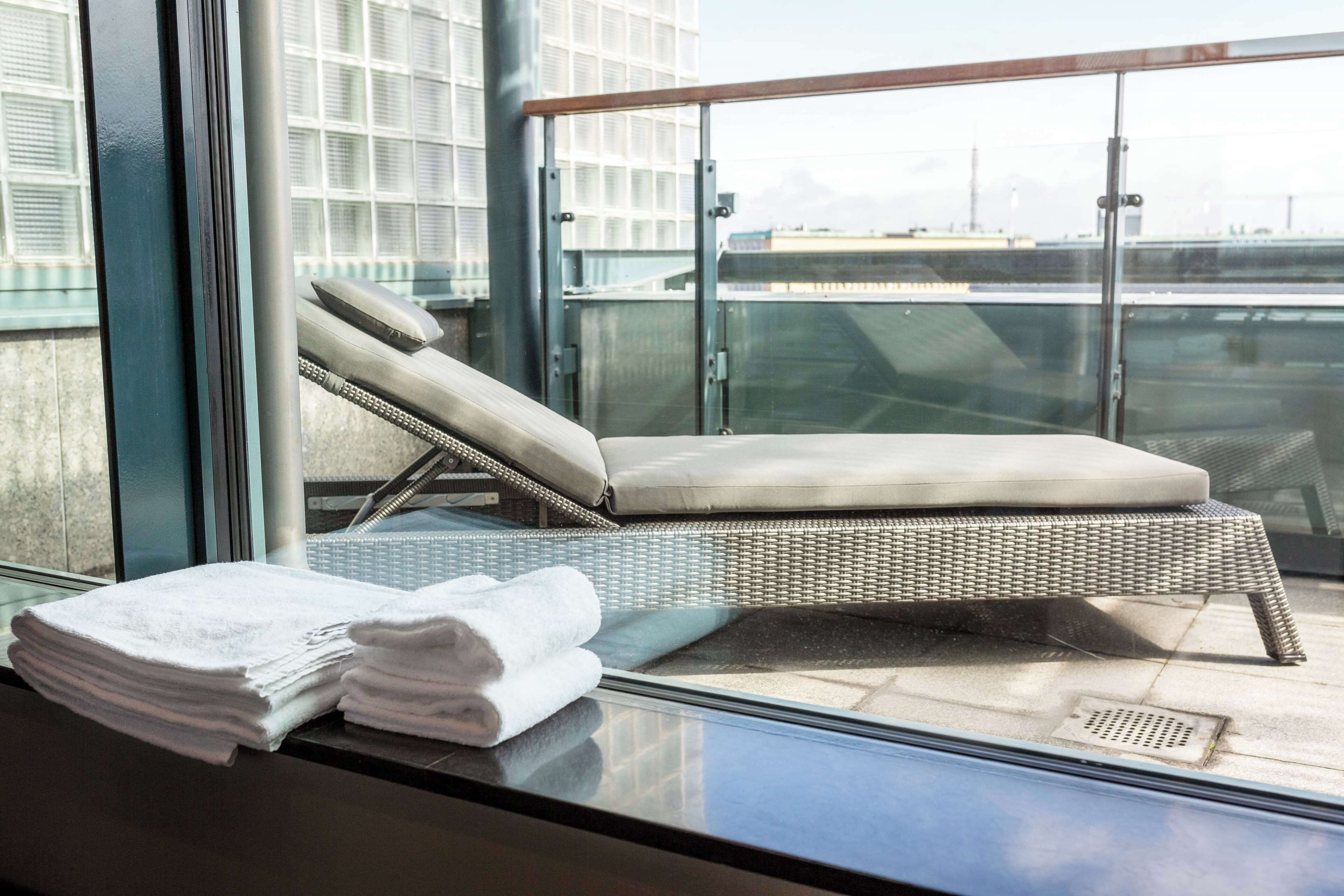 Een balkon met een rieten lounge stoel, een glazen hekwerk en een stap handdoeken.