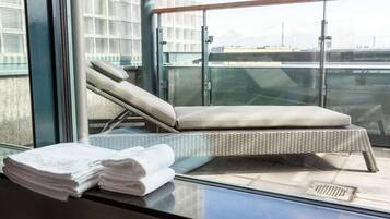 Een balkon met een rieten lounge stoel, een glazen hekwerk en een stap handdoeken.