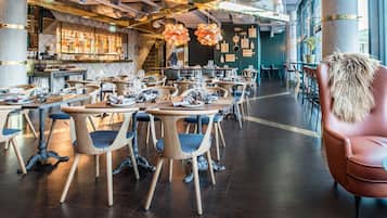 En rummelig restaurant med flere borde og stole, et barområde og store vinduer, der lukker naturligt lys ind.