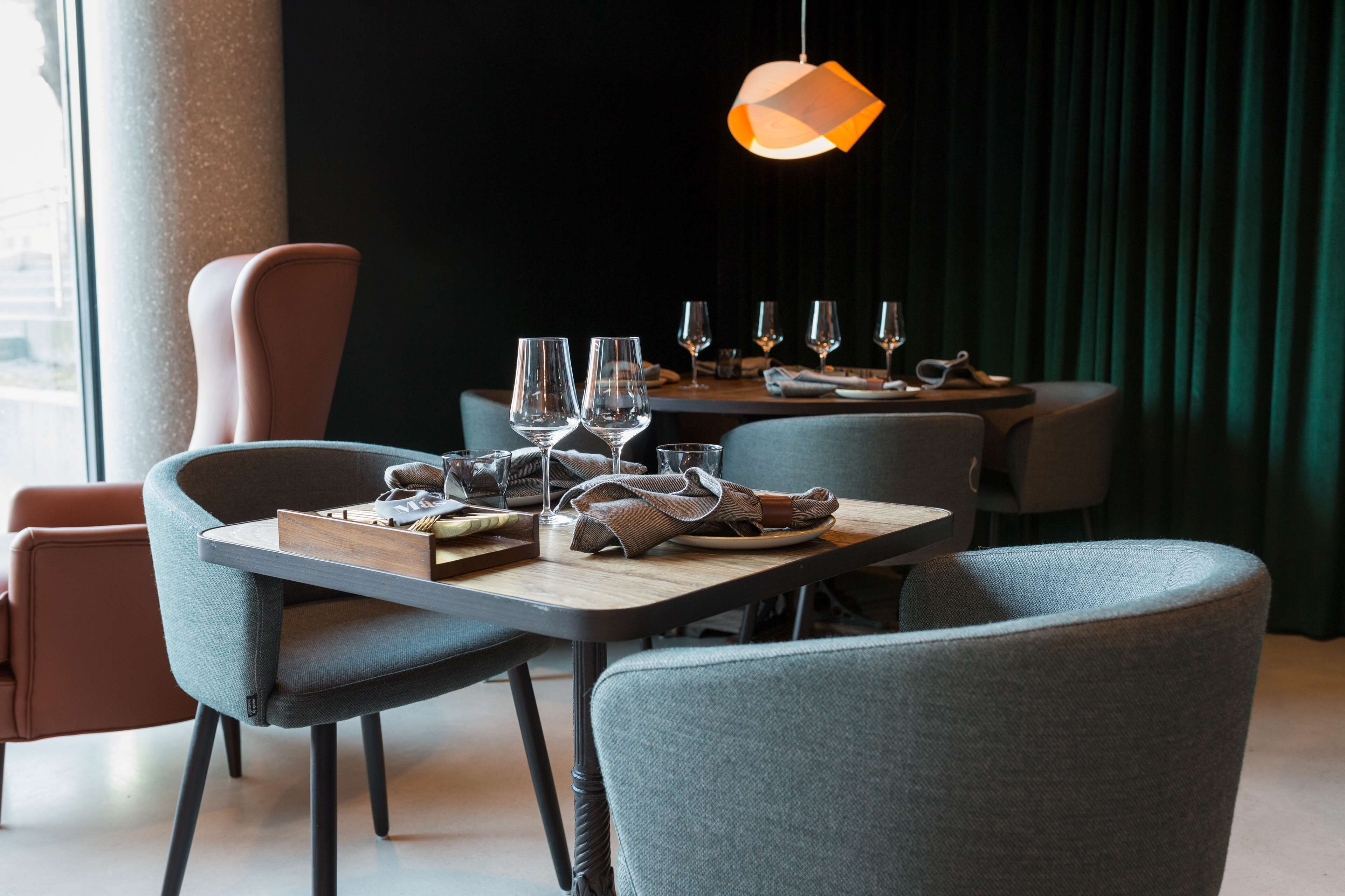 Un comedor con una mesa dispuesta para dos personas, con un diseño moderno de silla y una lámpara colgante.