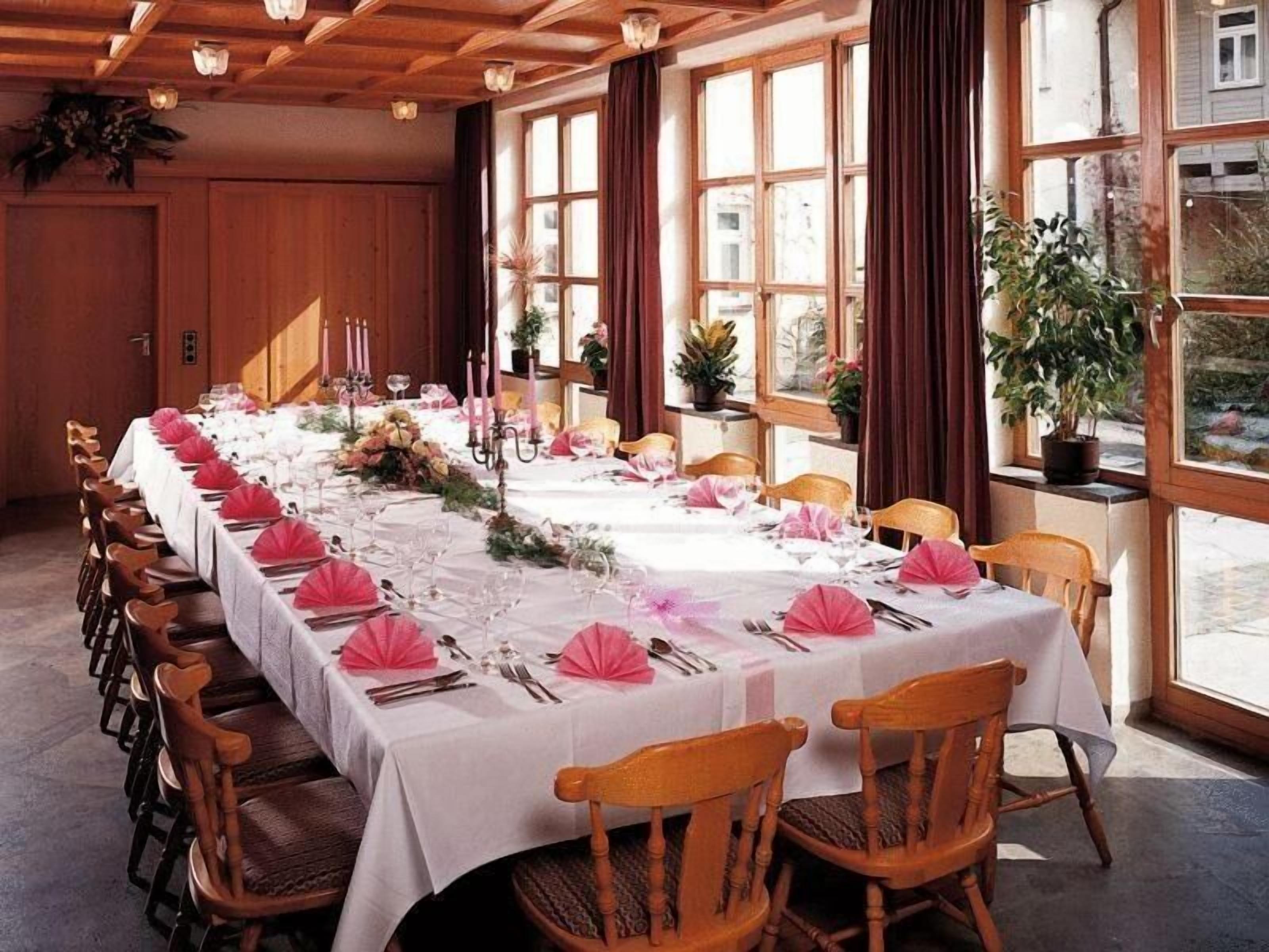 A long dining table set for a formal event with white tablecloths, pink napkins, and candles.