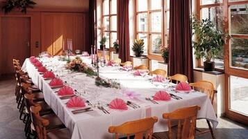 A long dining table set for a formal event with white tablecloths, pink napkins, and candles.