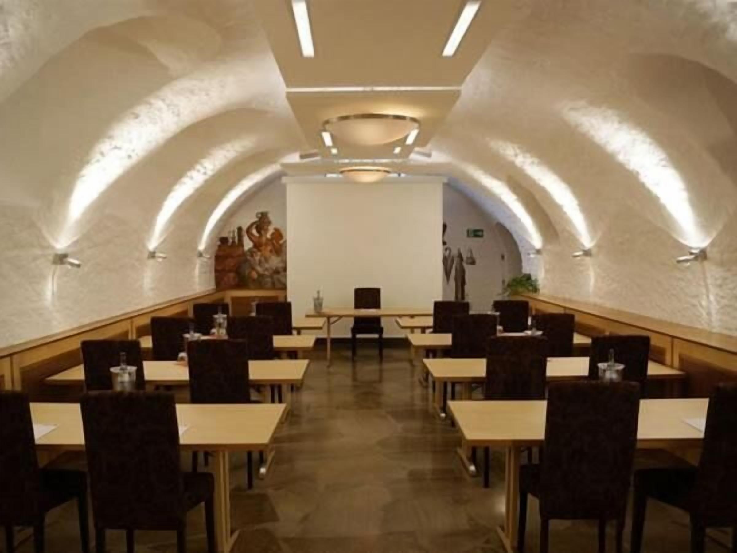 A conference room with tables and chairs arranged in a U-shape, a whiteboard at the front, and a mural on the wall.