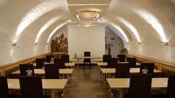 A conference room with tables and chairs arranged in a U-shape, a whiteboard at the front, and a mural on the wall.