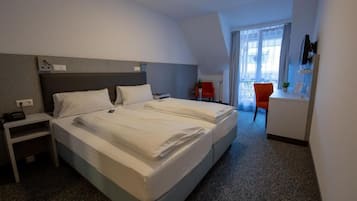 A hotel room with a large bed, a desk with a chair, and a window with curtains.