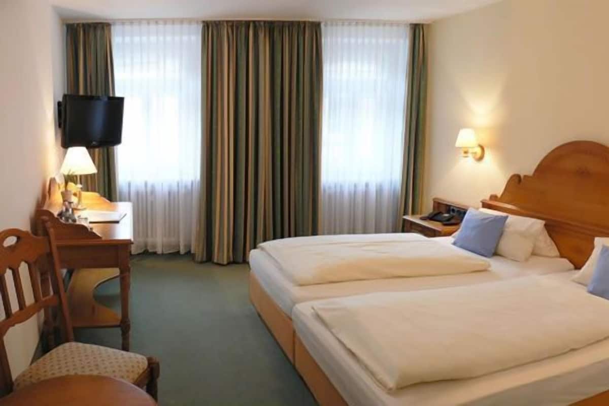 A hotel room with two beds, a desk, a chair, a TV, and curtains.