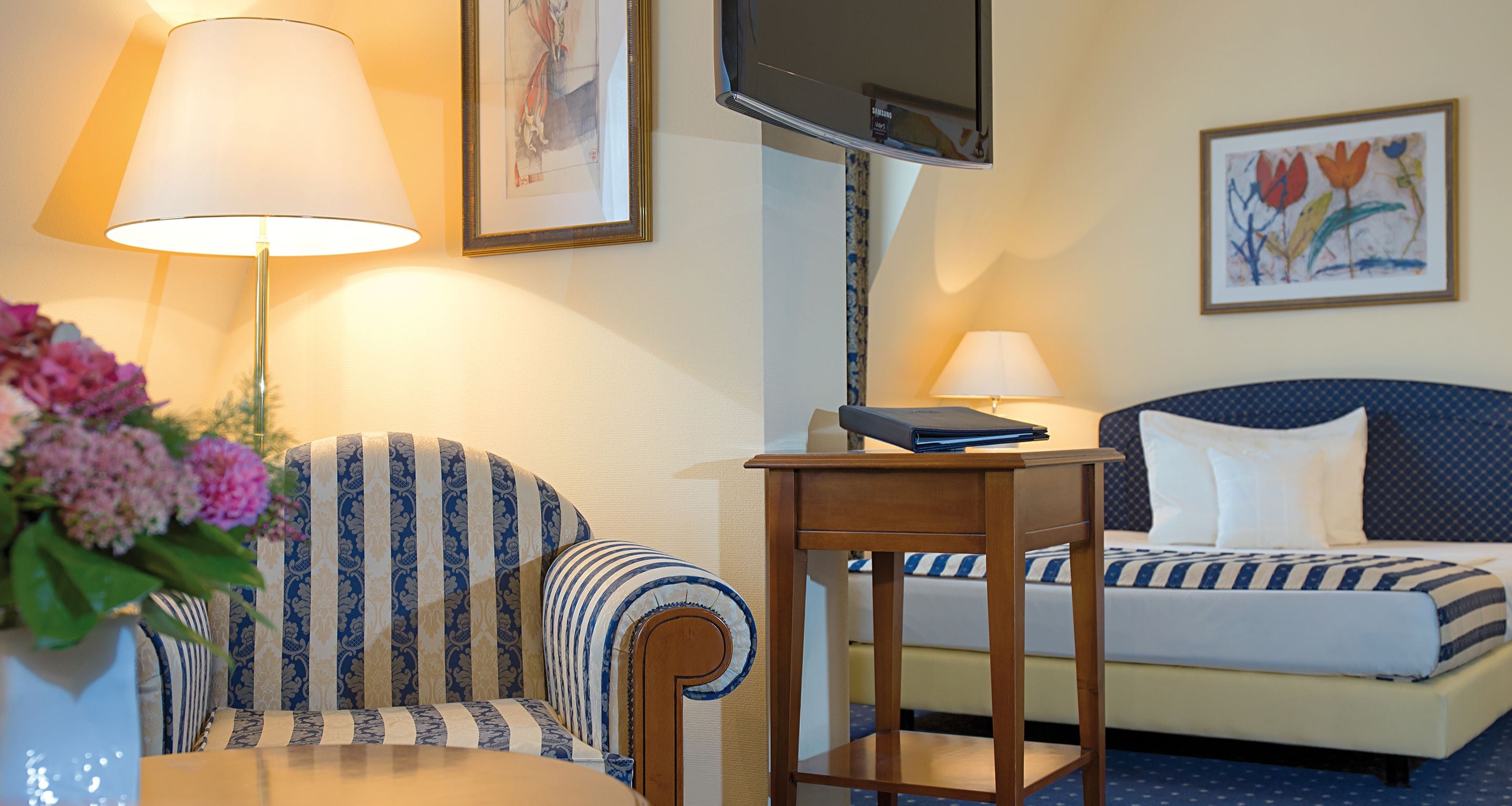A hotel room with a bed, a chair, a small table, a TV, and a lamp.