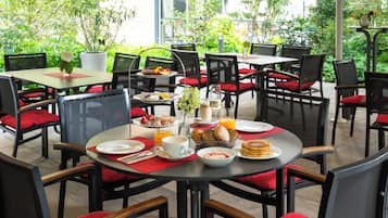 Une table de salle à manger ronde, entourée de chaises à coussins rouges, le tout agrémenté de verdure.