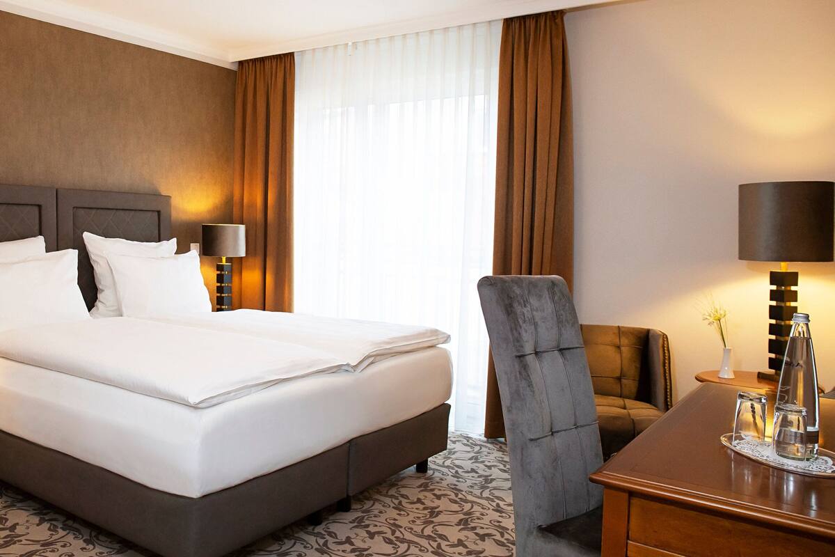 A hotel room with a large bed, two bedside tables with lamps, a chair, and a desk with a lamp.